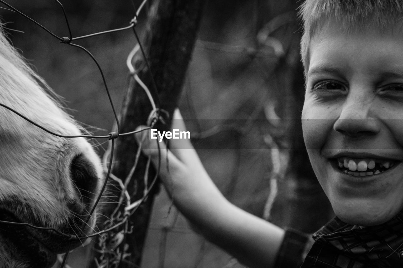 Close-up portrait of smiling boy with horse by fence