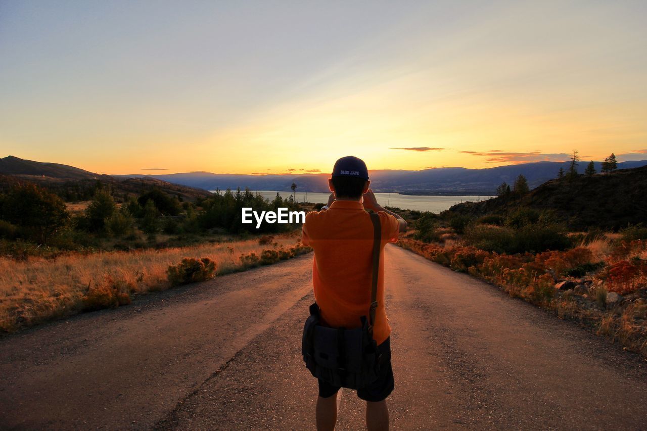 FULL LENGTH REAR VIEW OF MAN WALKING ON ROAD