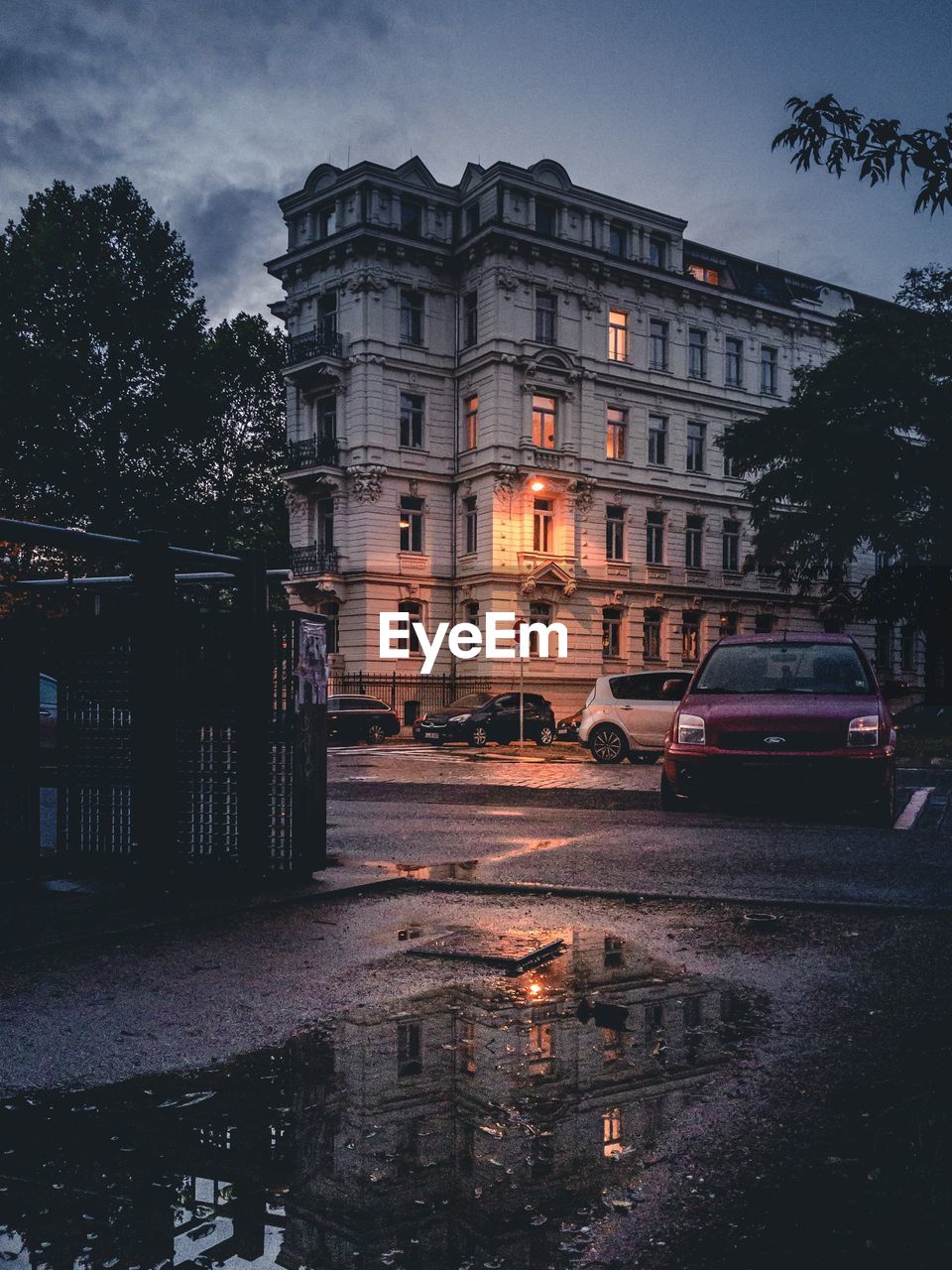 WET STREET BY BUILDINGS IN CITY DURING RAINY SEASON AT DUSK