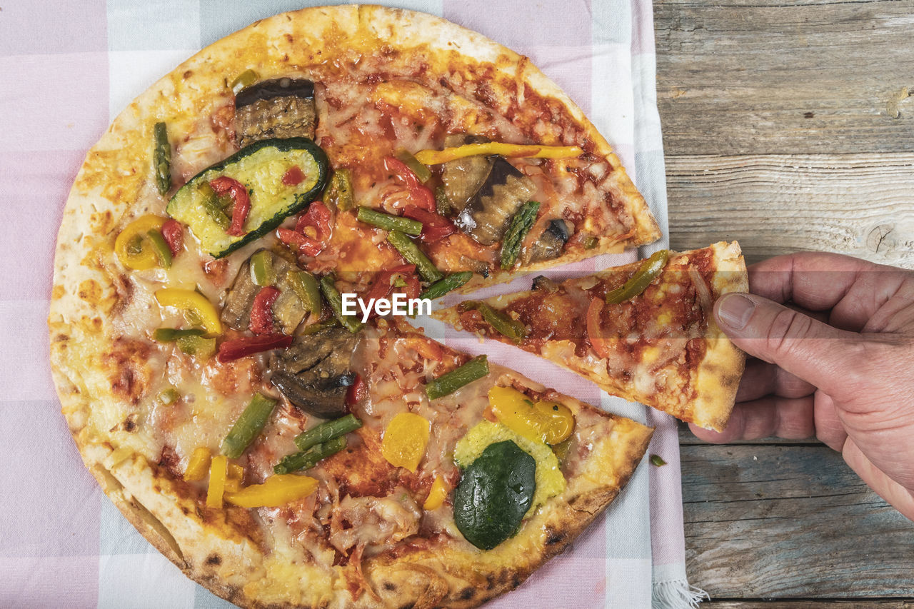 food, food and drink, pizza, hand, fast food, freshness, one person, dish, italian food, vegetable, cuisine, cheese, holding, unhealthy eating, high angle view, dairy, fruit, table, indoors, slice, directly above, close-up, lifestyles, wood, tomato, personal perspective, pizza box, baked, olive