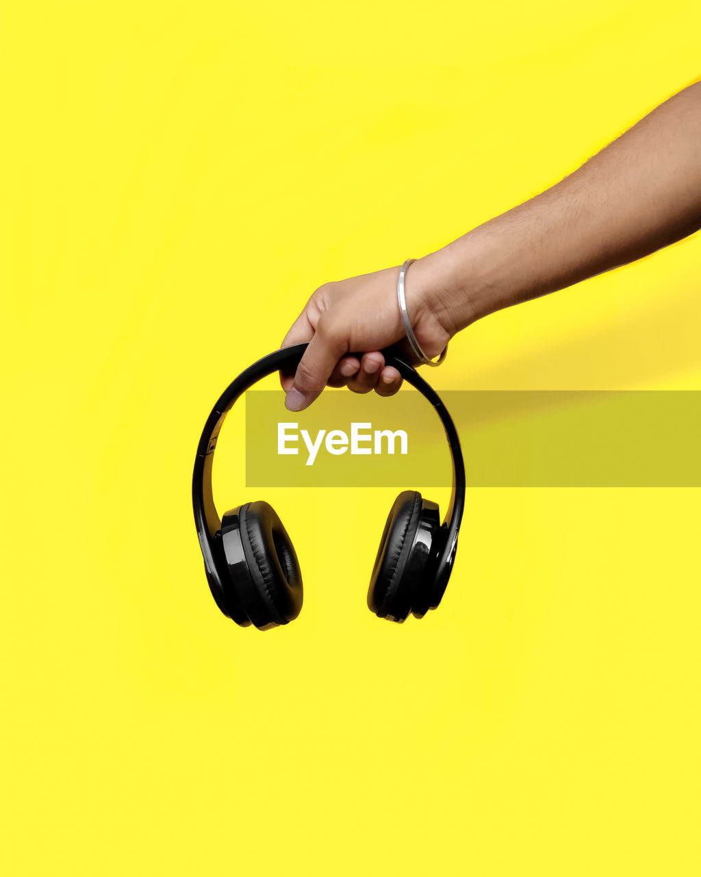 Cropped hand of man holding headphones against yellow background