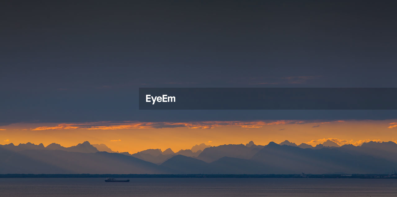 SCENIC VIEW OF SEA AND SILHOUETTE MOUNTAINS AGAINST SKY AT SUNSET