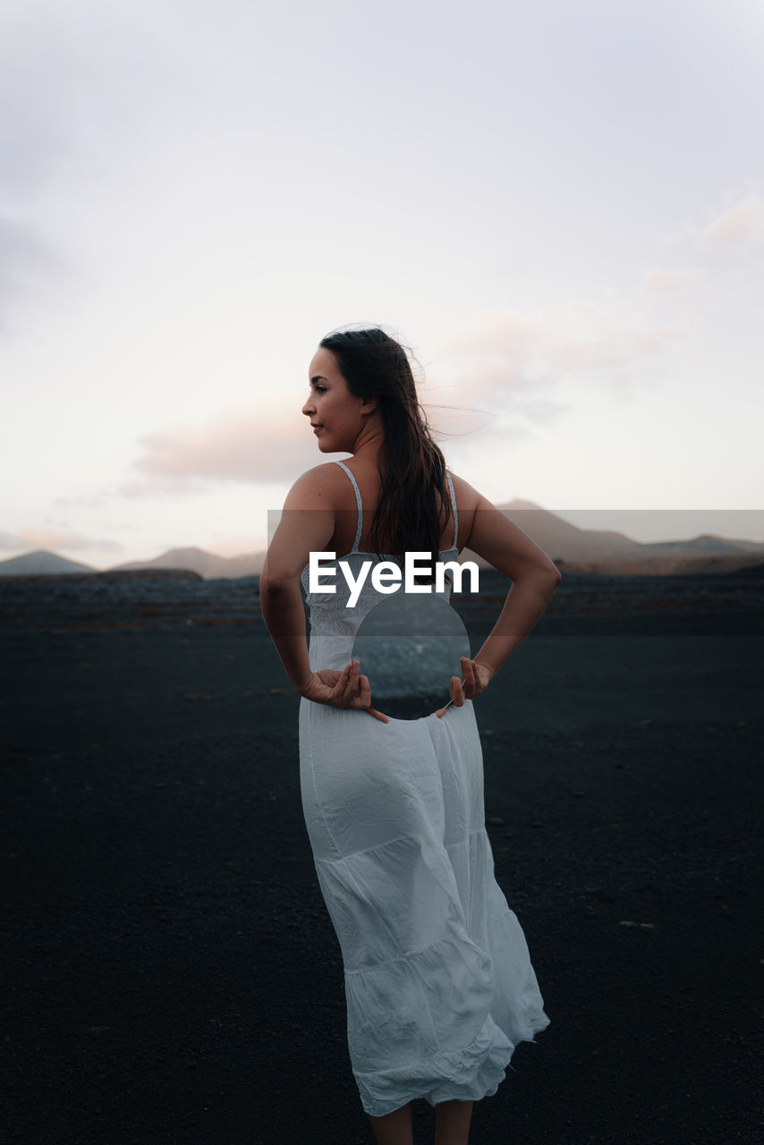 Young woman standing on land against sky during sunset