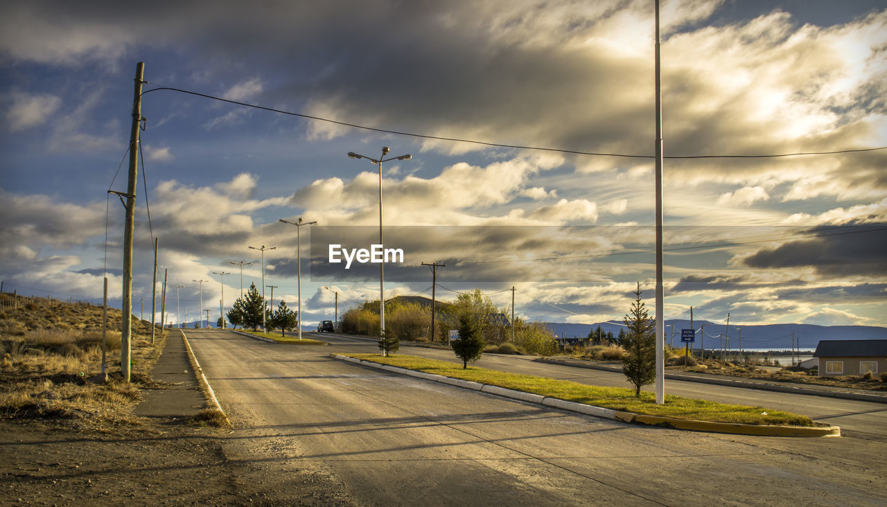 Road amidst field against cloudy sky