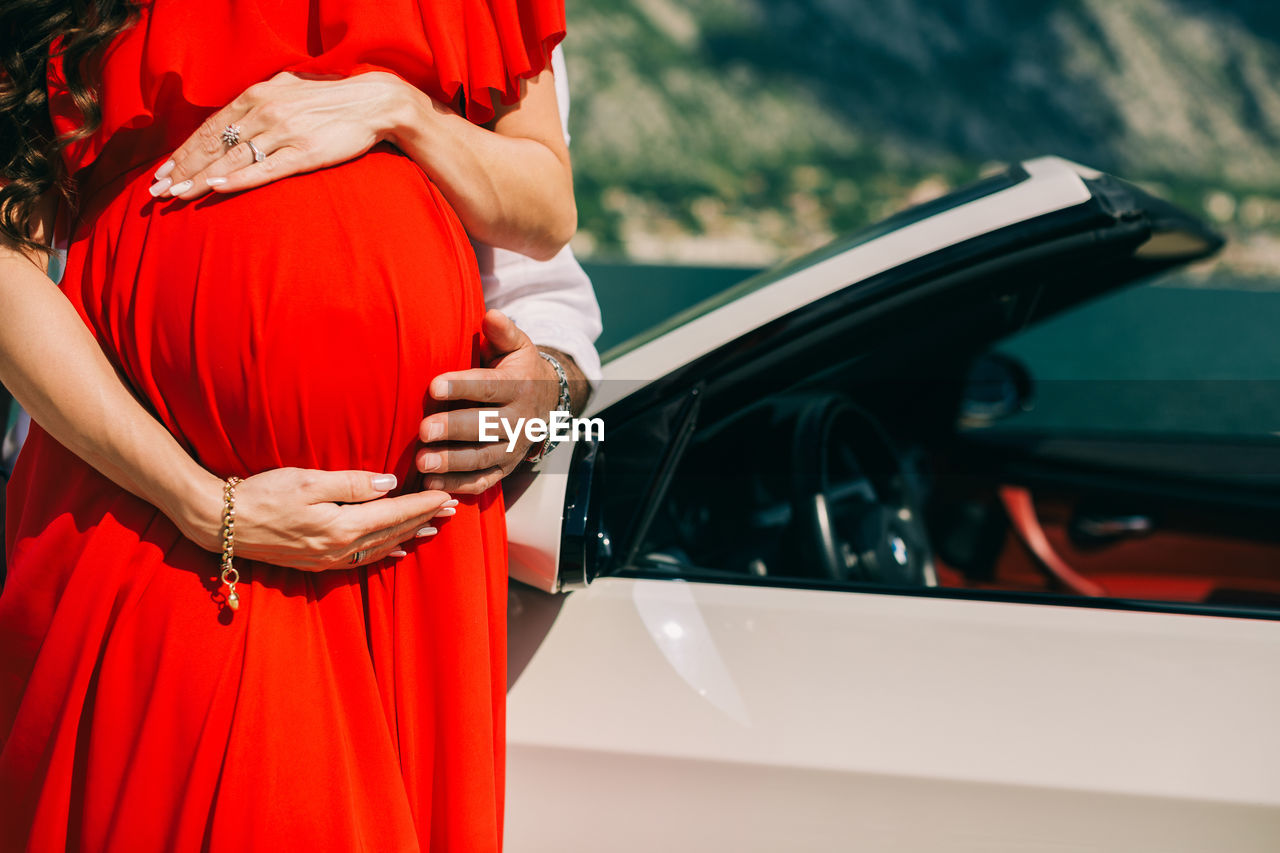 Cropped hand of man touching stomach of pregnant woman by car