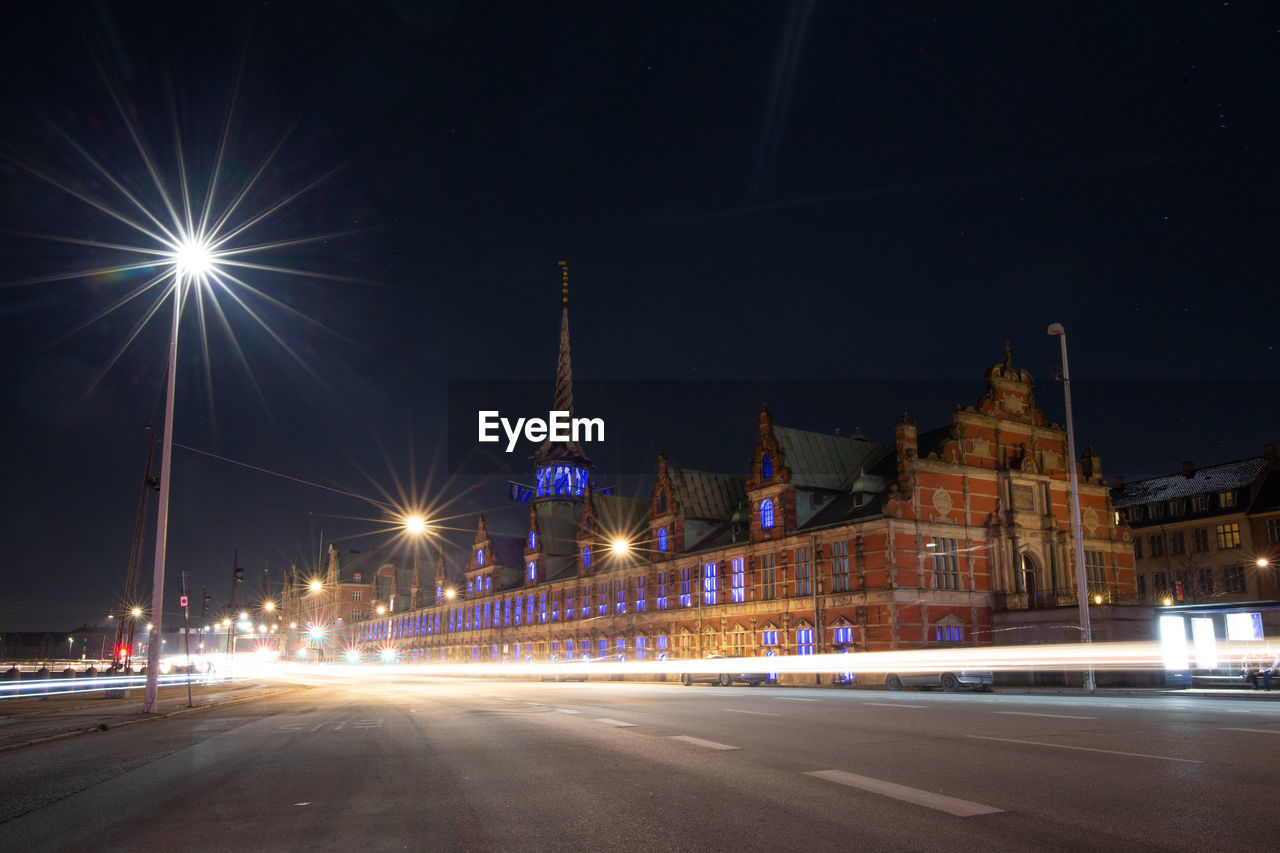 ILLUMINATED LIGHT TRAILS ON STREET AGAINST BUILDINGS AT NIGHT