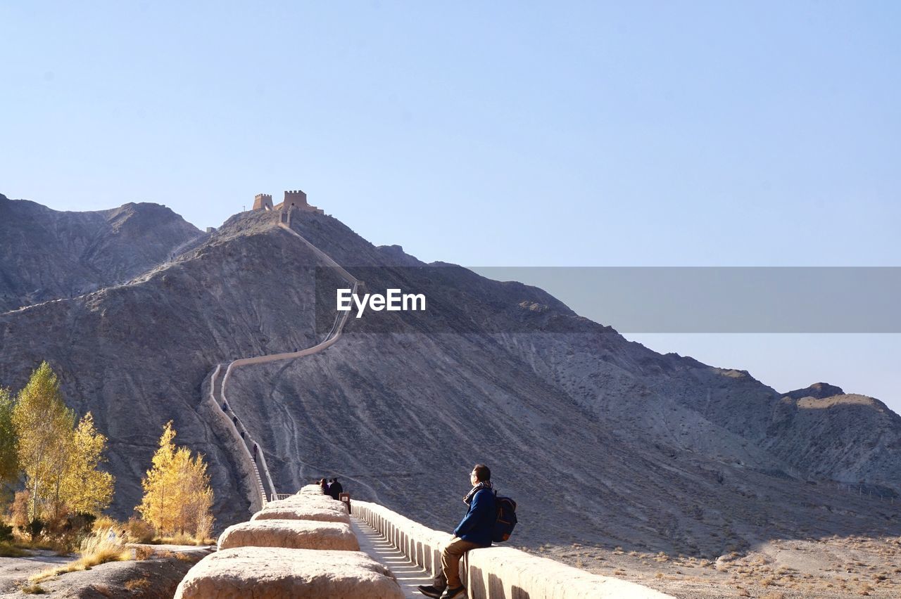 REAR VIEW OF MAN SITTING ON ROCK