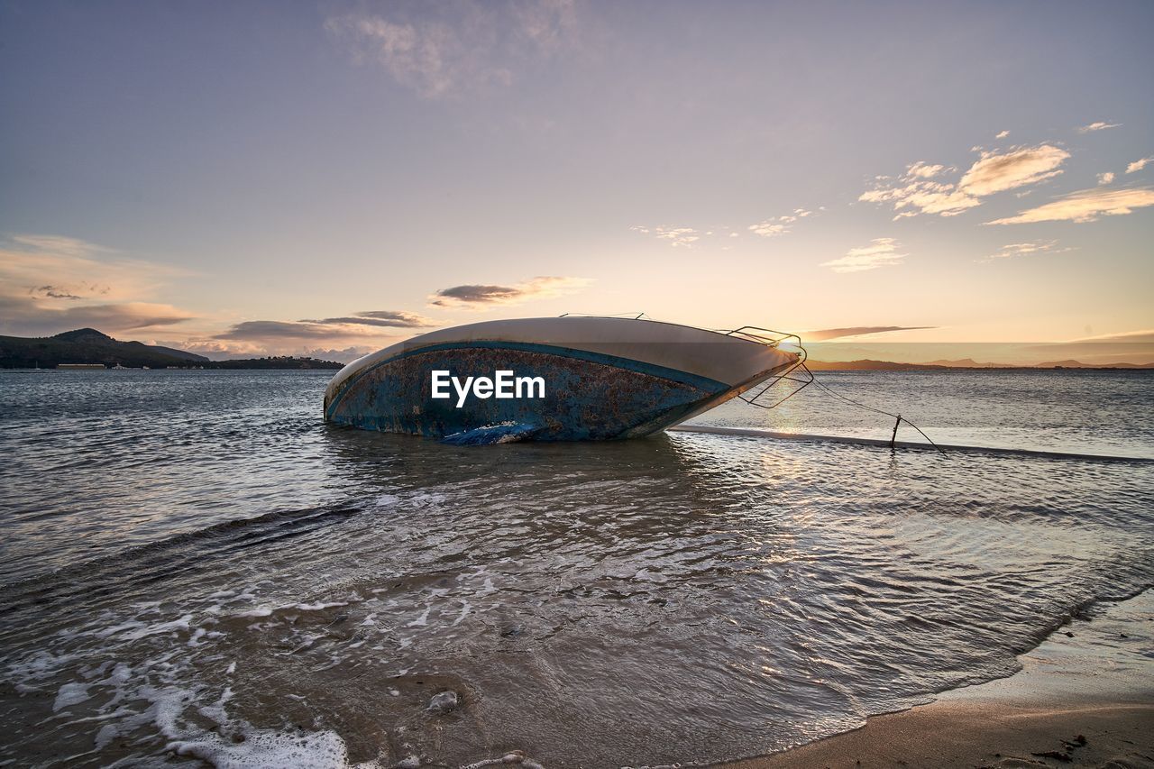 BOAT MOORED ON SHORE AGAINST SKY DURING SUNSET