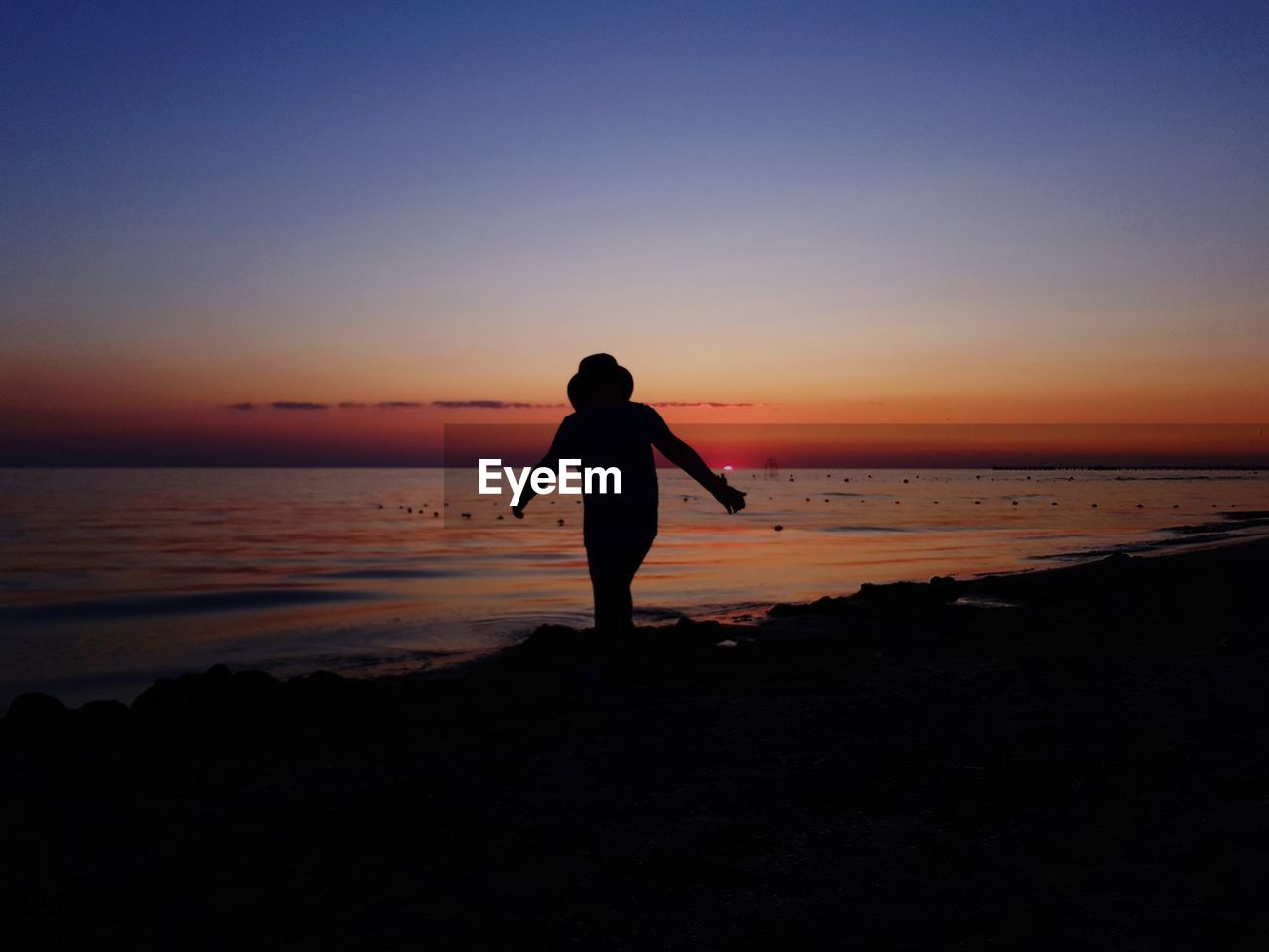 SILHOUETTE MAN STANDING ON BEACH DURING SUNSET