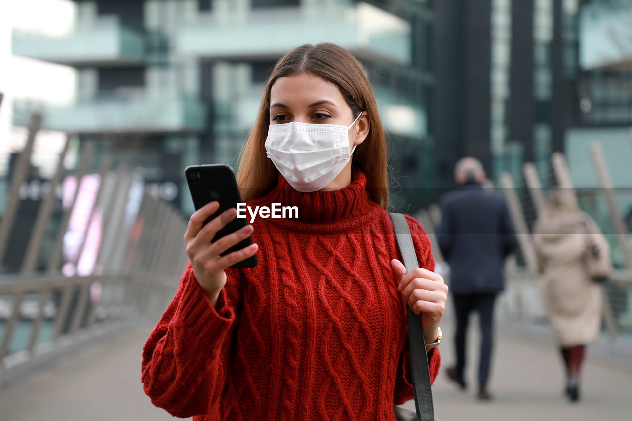 Woman wearing mask using smart phone standing outdoors