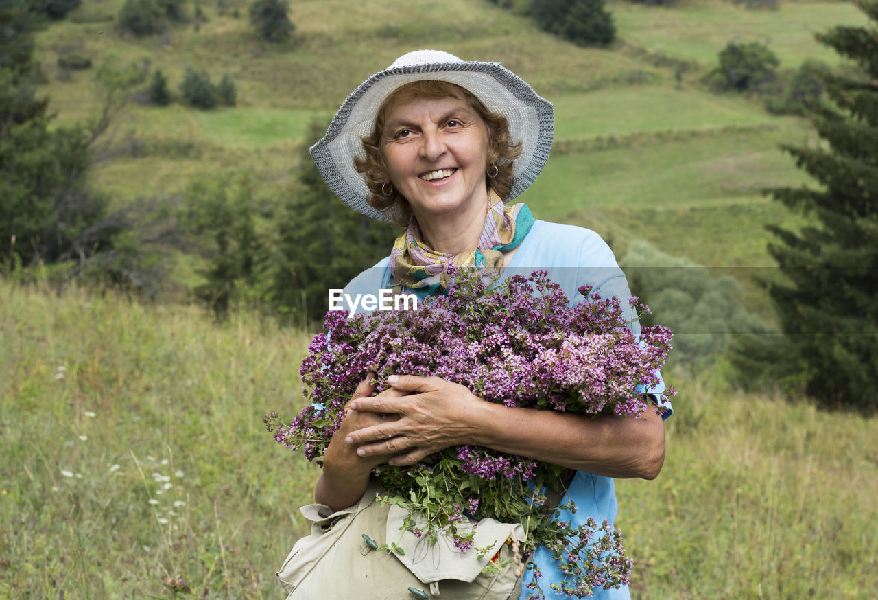 Portrait of a smiling young woman with oregano herbs flowers in her hands, beautiful nature