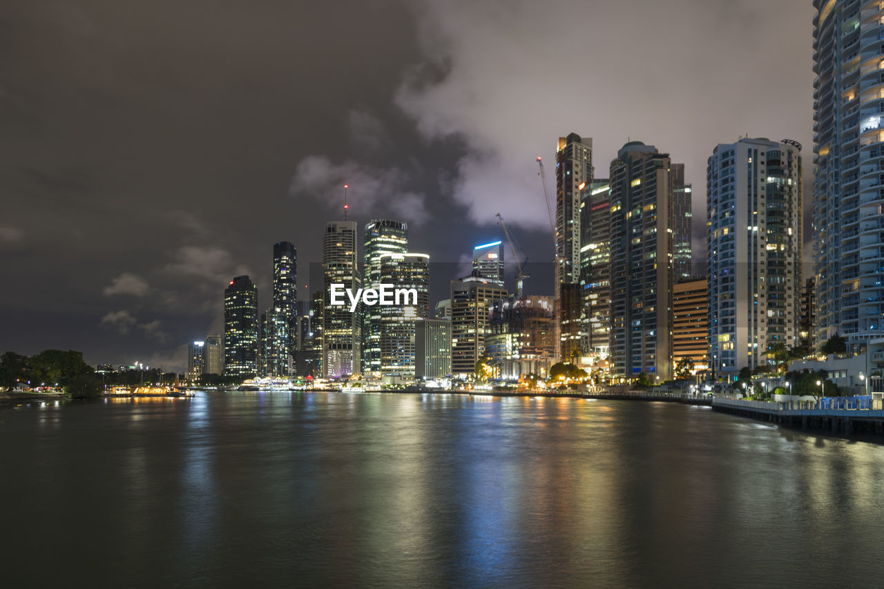 Illuminated city by sea against sky at night