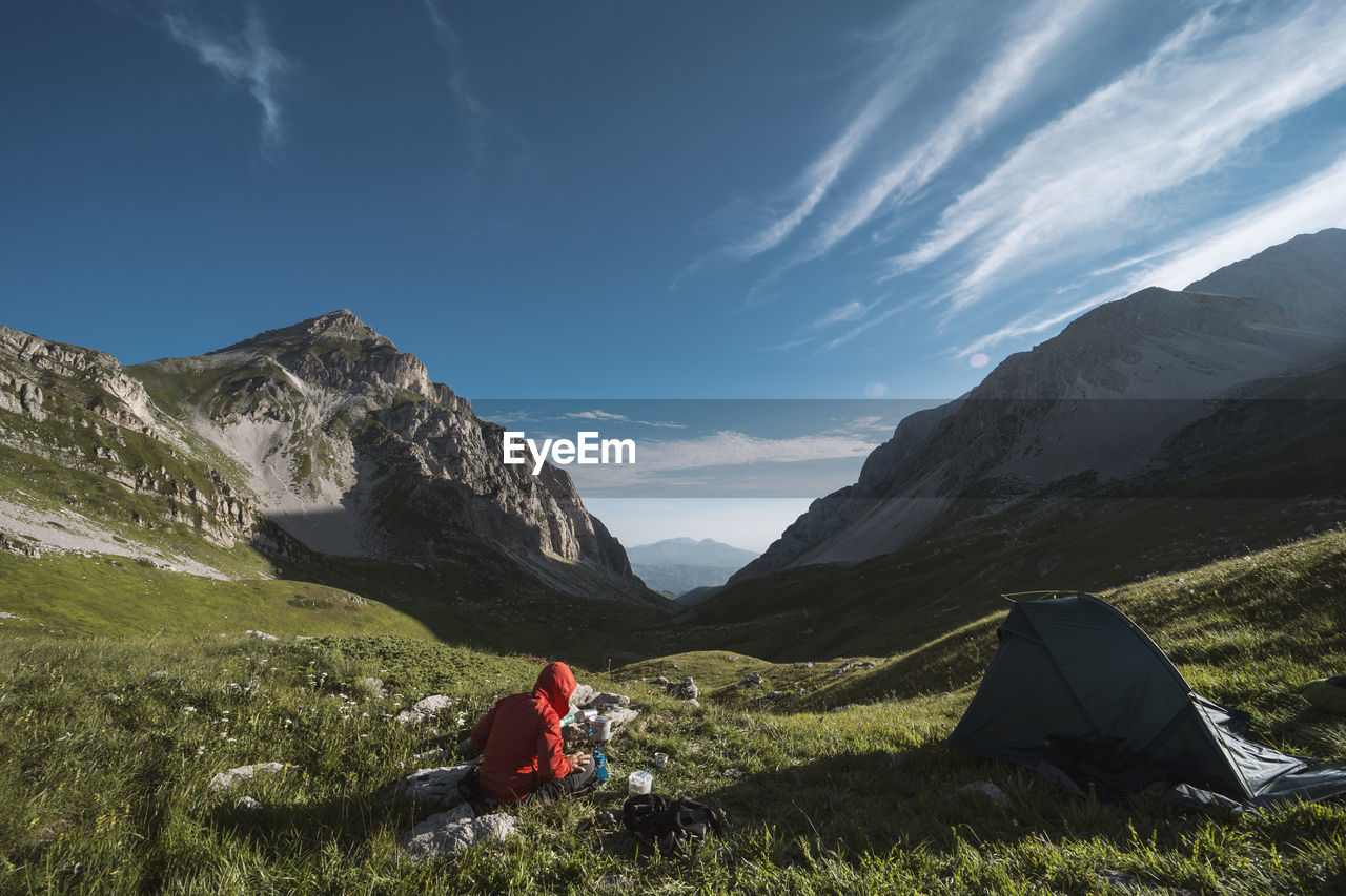 Man sitting on mountain against sky