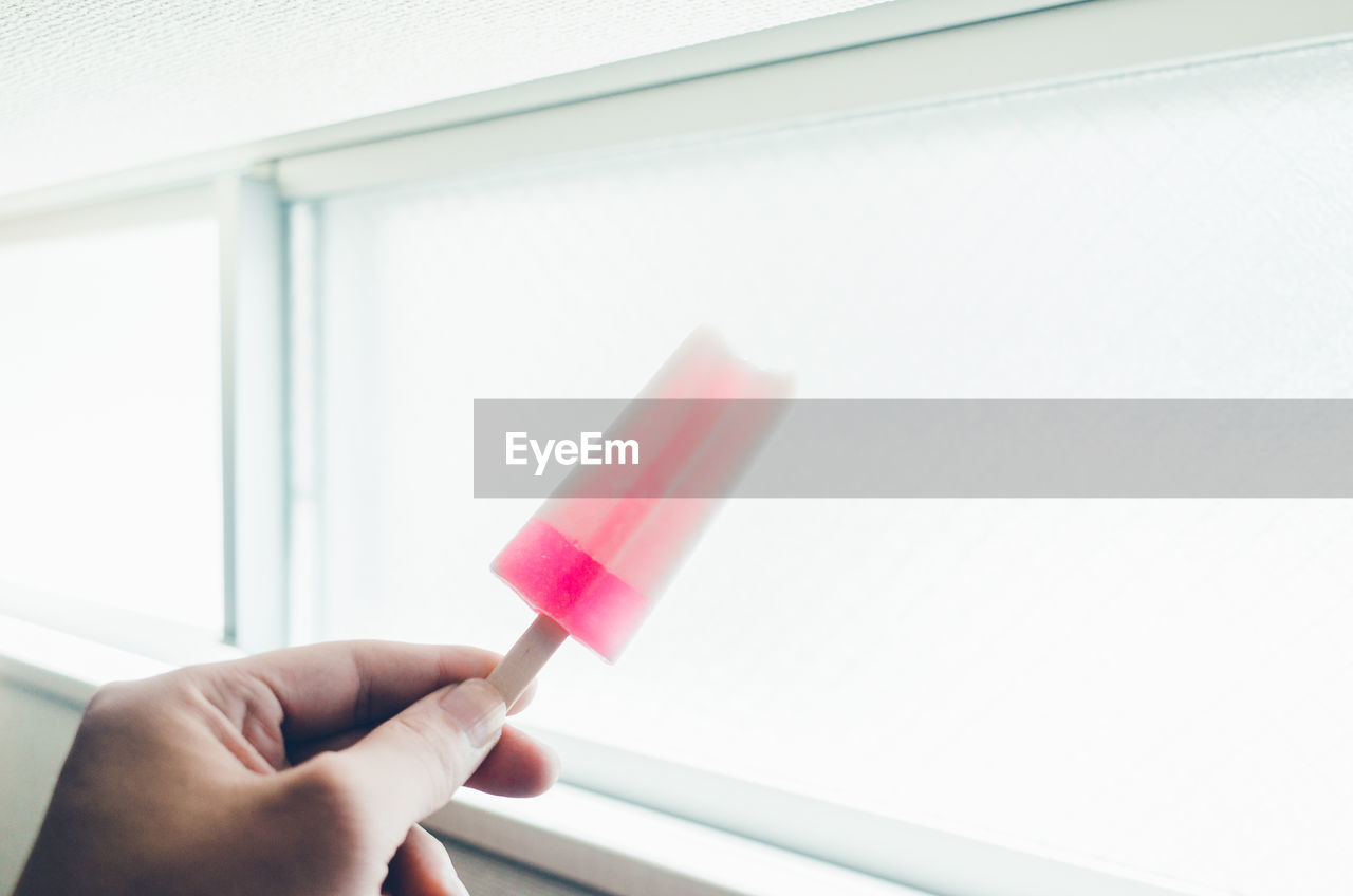 Cropped hand of woman holding flavored ice against window