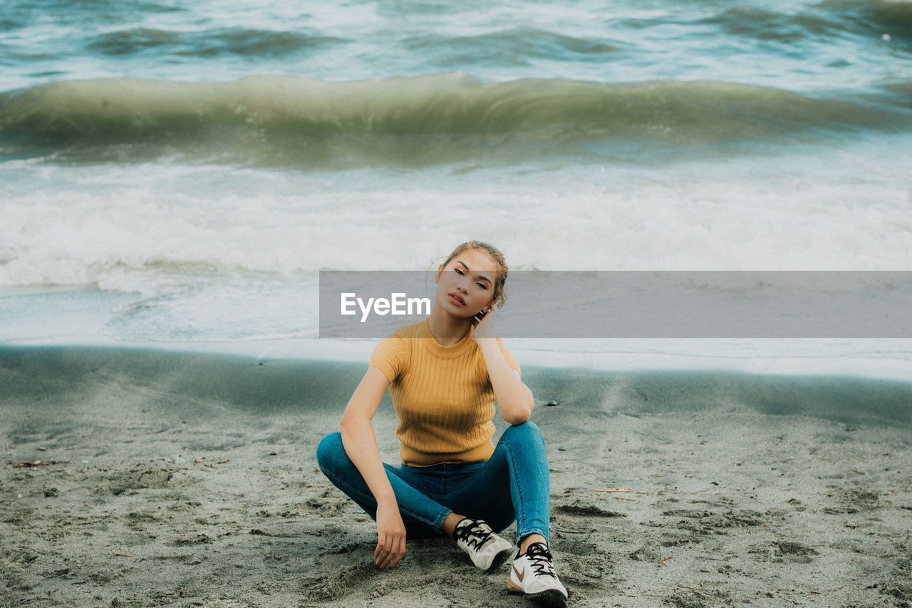 PORTRAIT OF HAPPY WOMAN SITTING ON BEACH