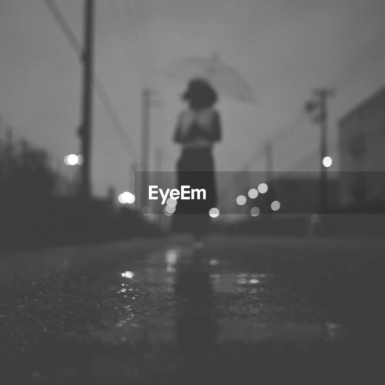 Woman with umbrella standing on street during rainy season at dusk