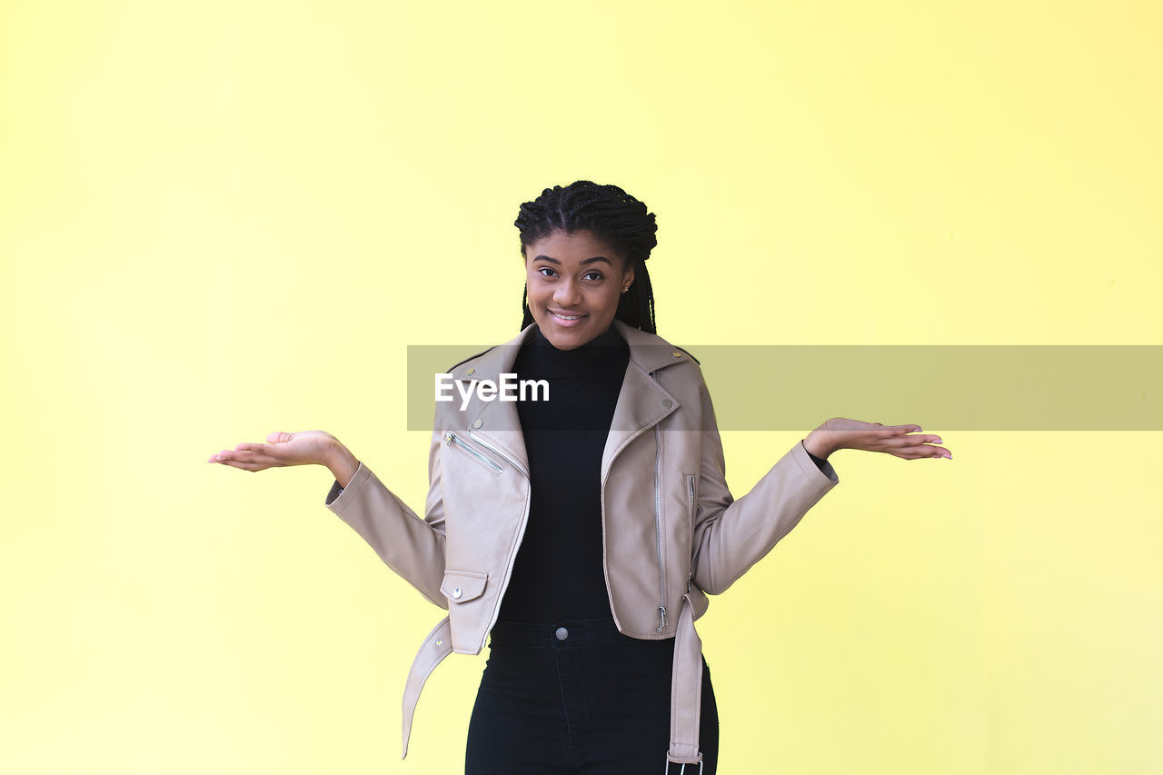 PORTRAIT OF SMILING YOUNG WOMAN AGAINST WALL