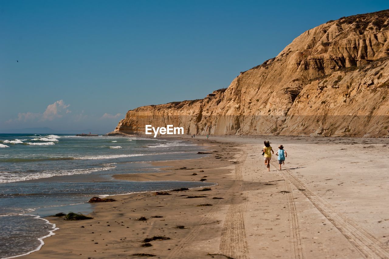 Children running at beach against sky