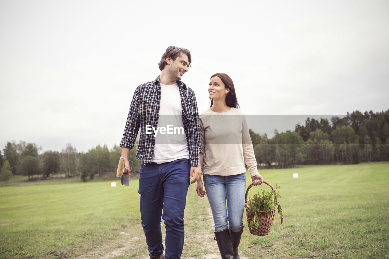 Loving couple with basket and gardening tool walking on field