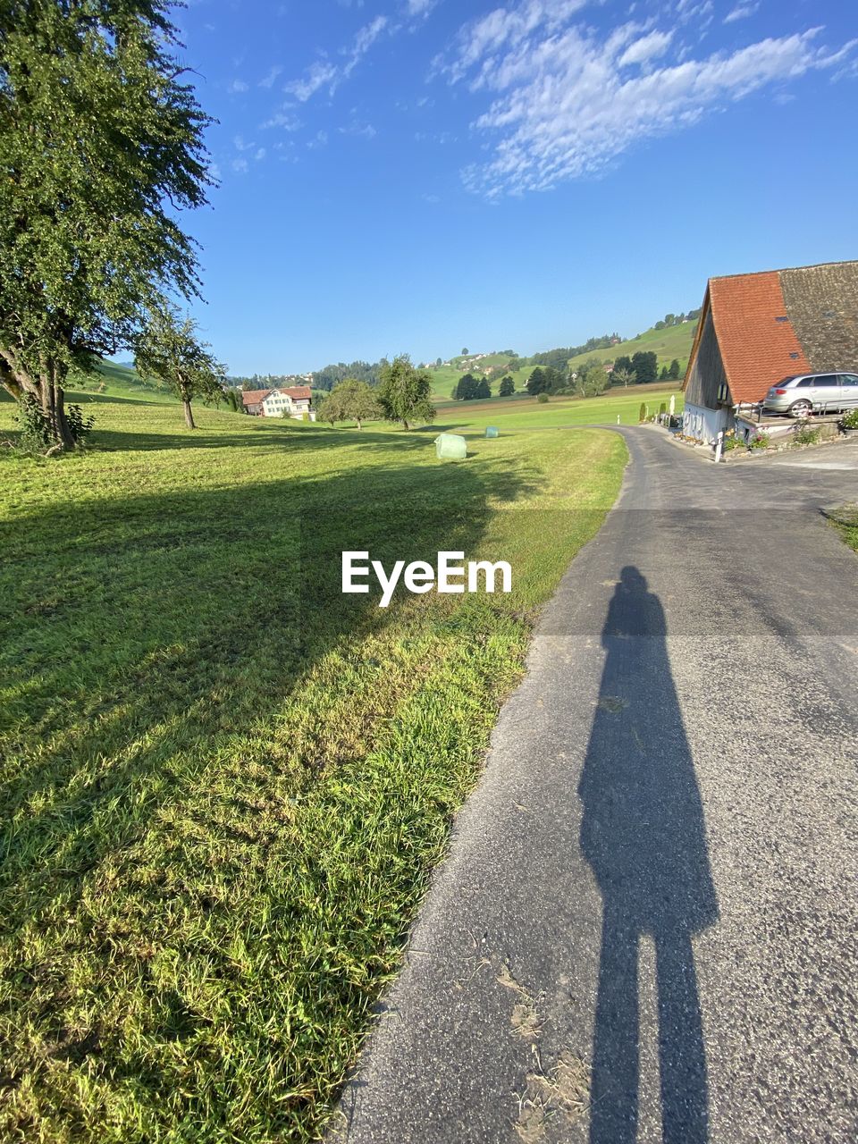 SHADOW OF PERSON ON ROAD AMIDST FIELD
