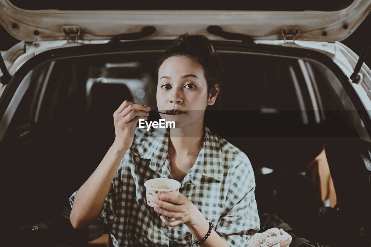 Young woman sitting on trunk and eatting dessert