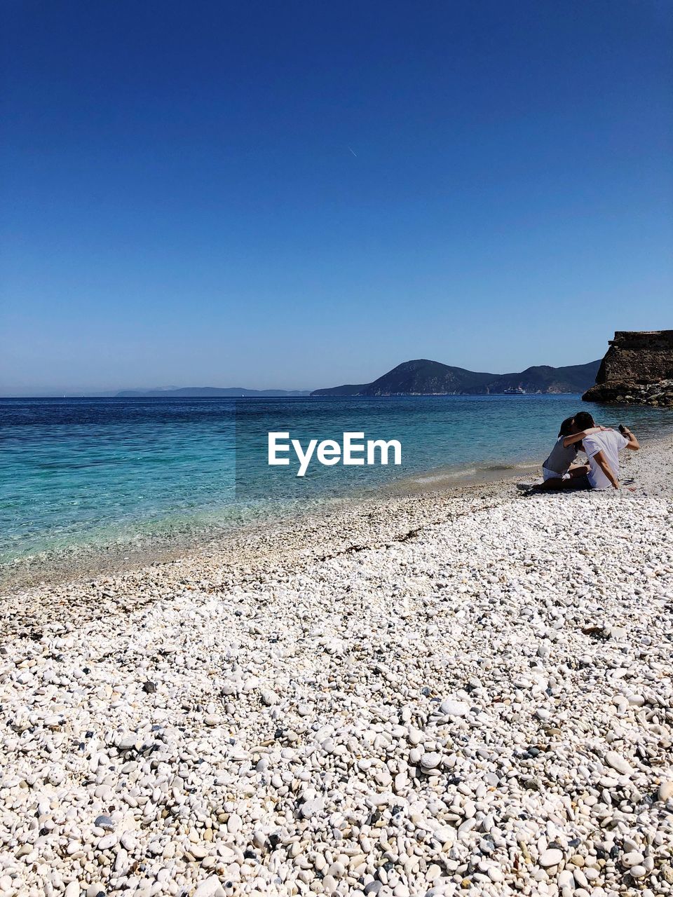 WOMAN SITTING ON BEACH AGAINST CLEAR SKY