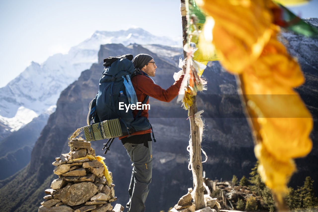 Side view of male hiker hanging buddhist prayer flag on rope during trekking in himalayas mountains in nepal