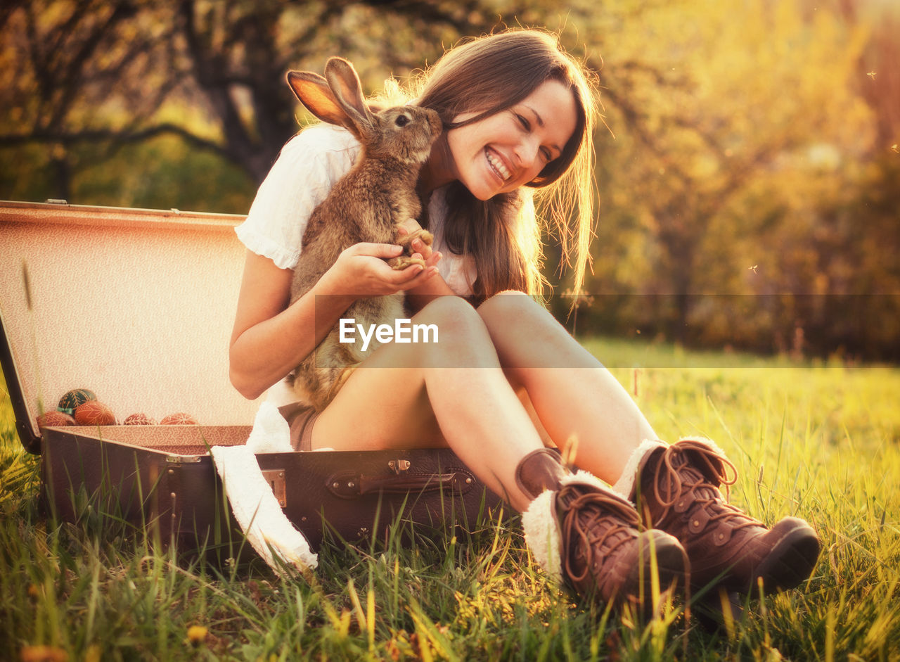 Young woman with rabbit sitting on field
