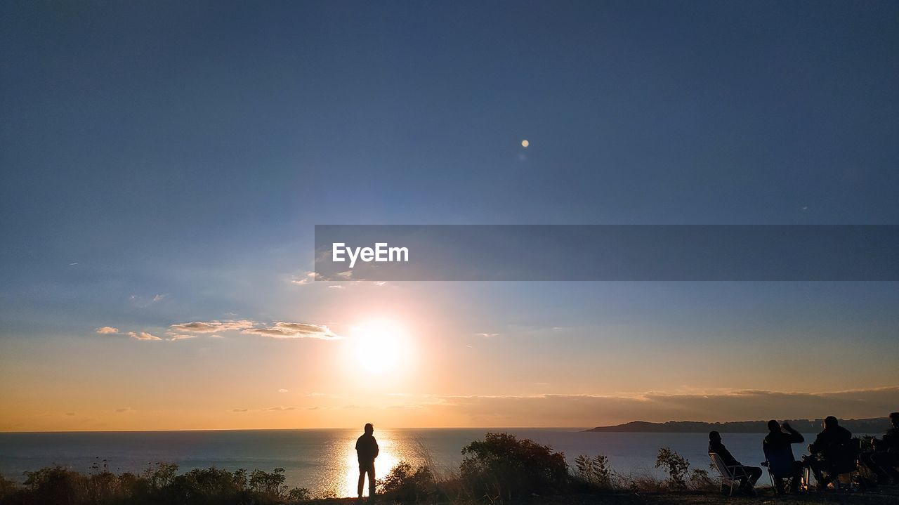 Rear view of woman standing on beach against sky during sunset