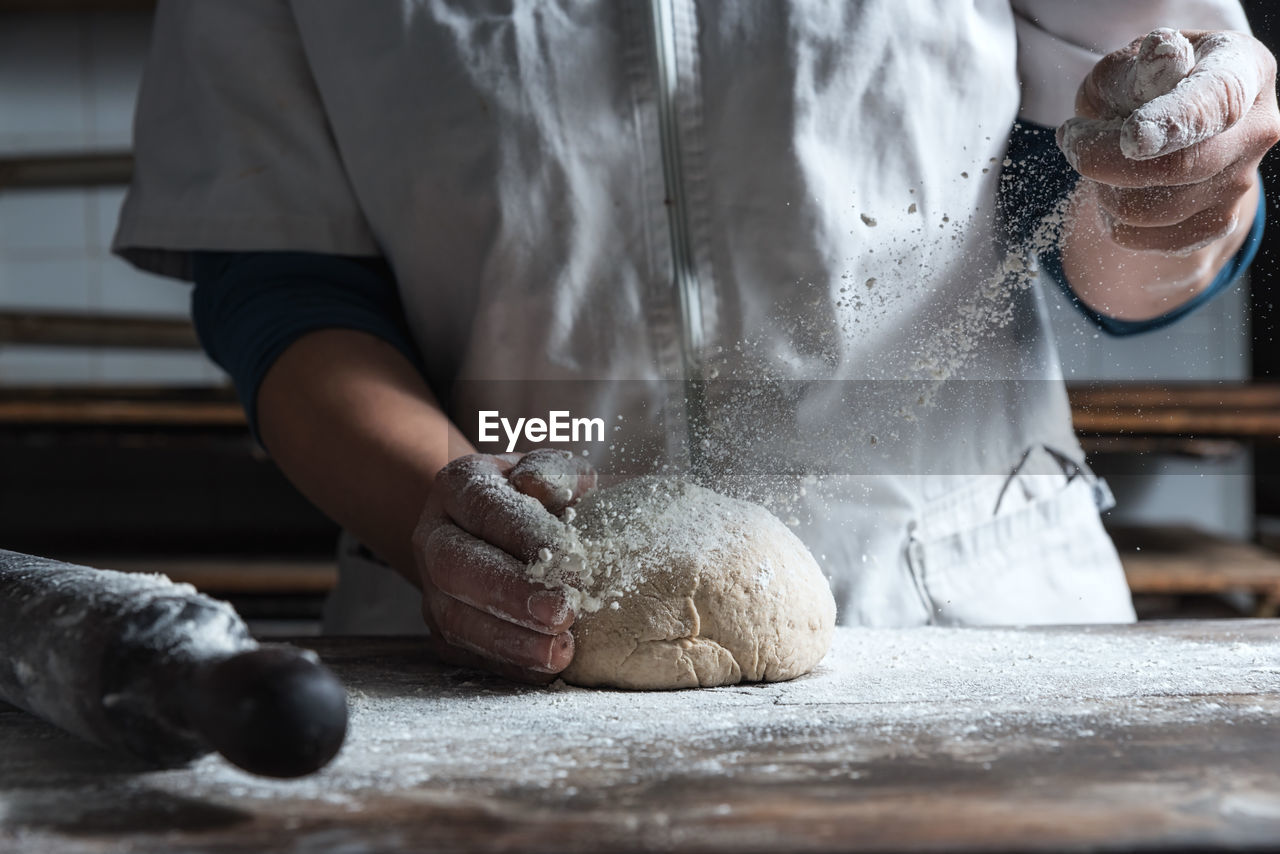 Unrecognizable person kneading dough with flour on table while working in bakery