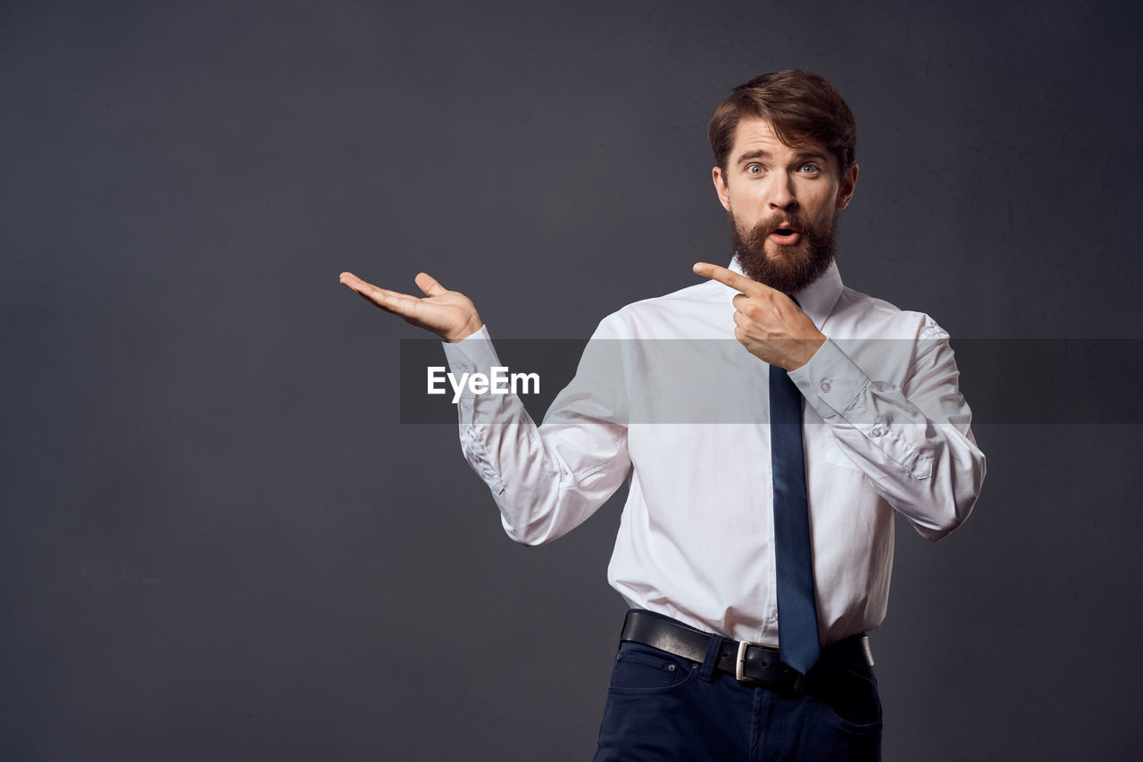 PORTRAIT OF MAN STANDING AGAINST GRAY BACKGROUND