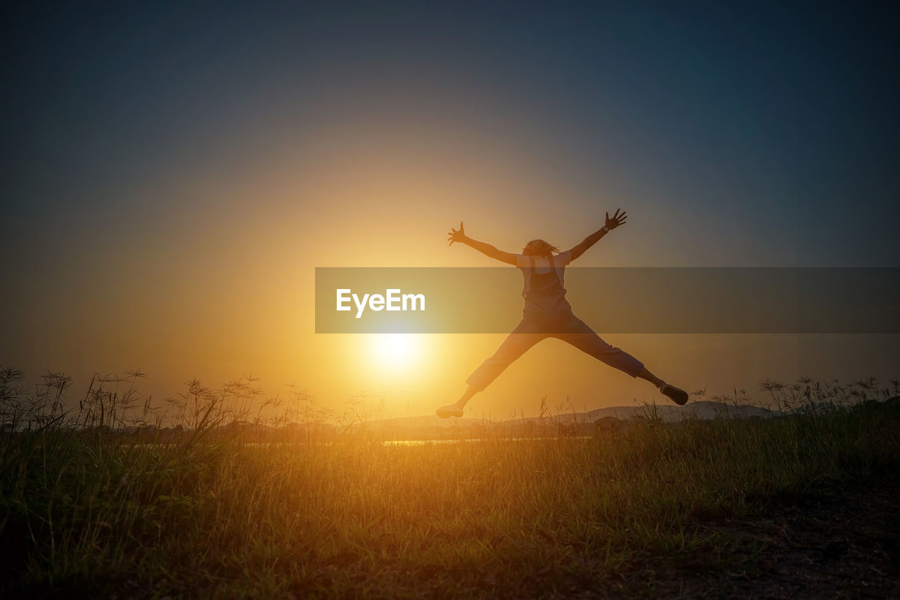 Woman jumping on field against sky during sunset