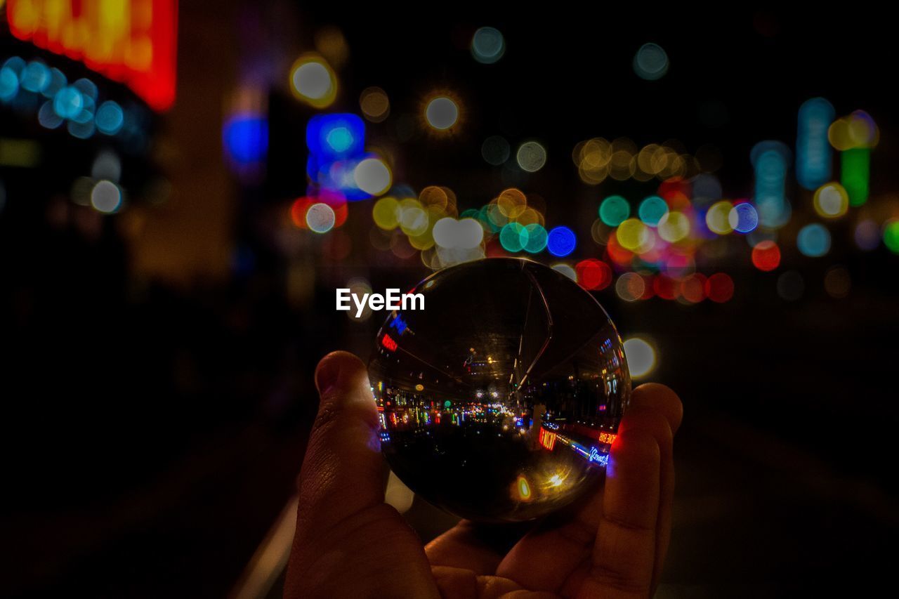 Close-up of person holding crystal ball against illuminated lights at night