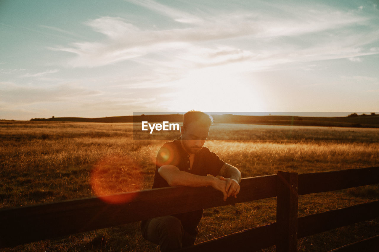 Man standing by railing at farm during sunset