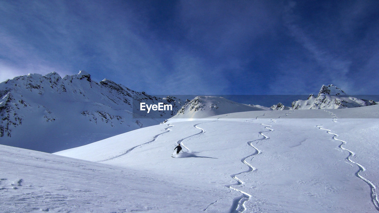 Person skiing on ski slope by snowcapped mountains against sky