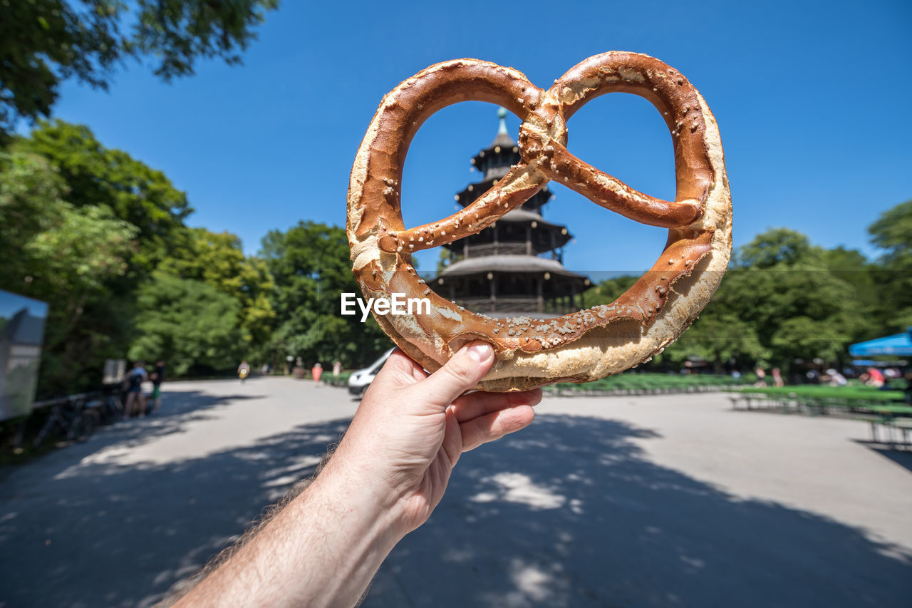 Close-up of hand holding pretzel against sky