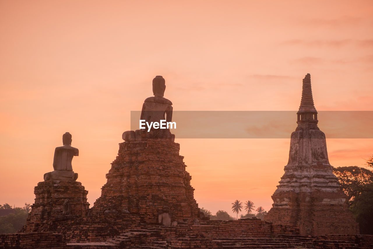 Low angle view of buddha statues and temple against sky during sunset