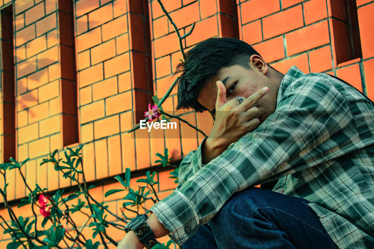 Portrait of young man showing middle finger outside building