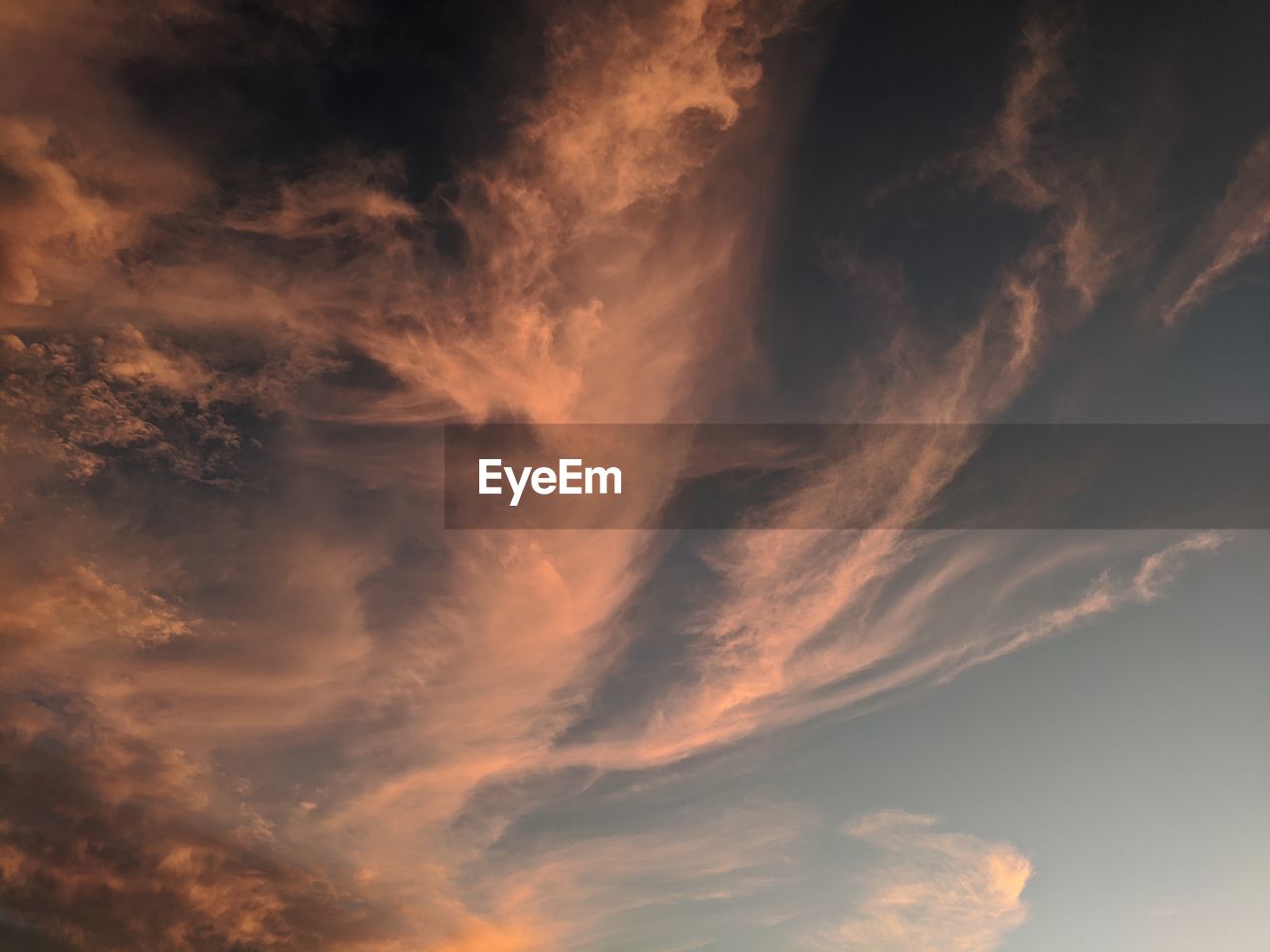 Low angle view of dramatic desert sky with swirly orange clouds at sunset