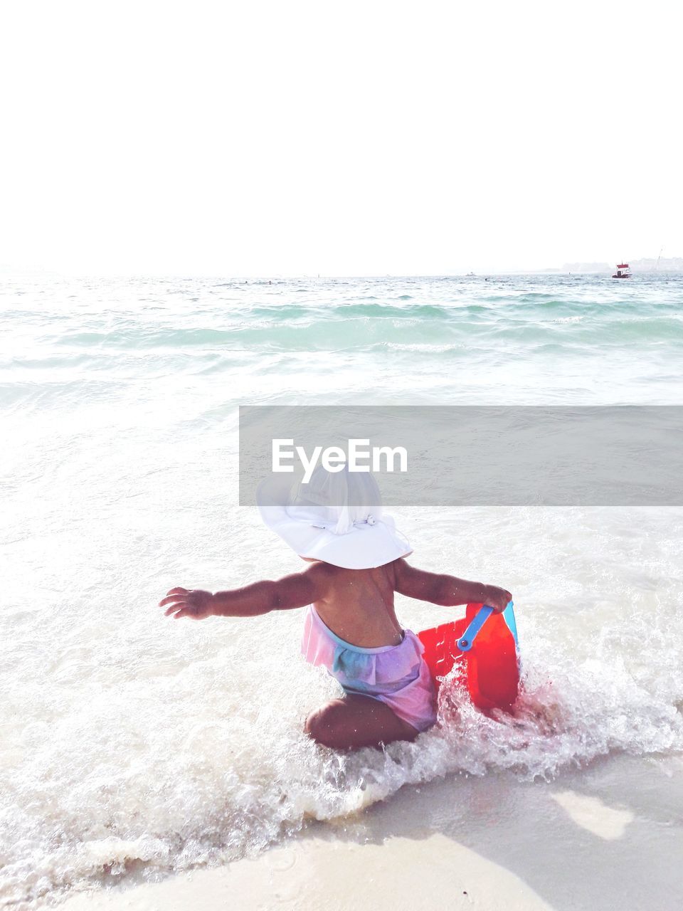 Rear view of girl holding bucket on shore at beach against sky