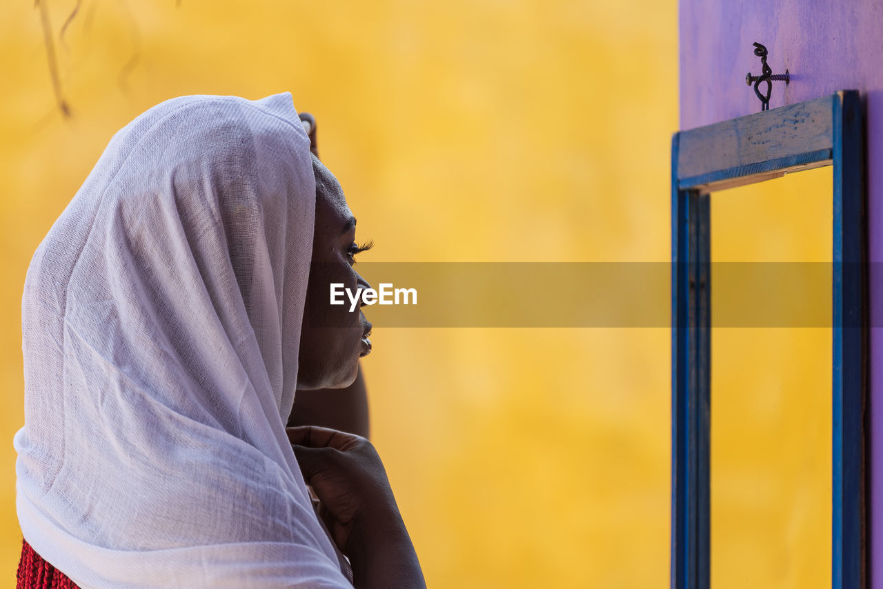 African ghana woman standing in front of a mirror with a white shawl covering her hair