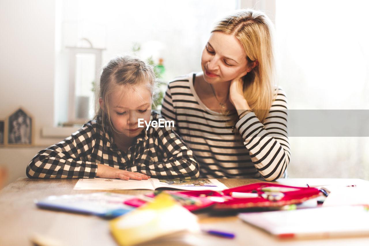 Girl studying while sitting with mother at home