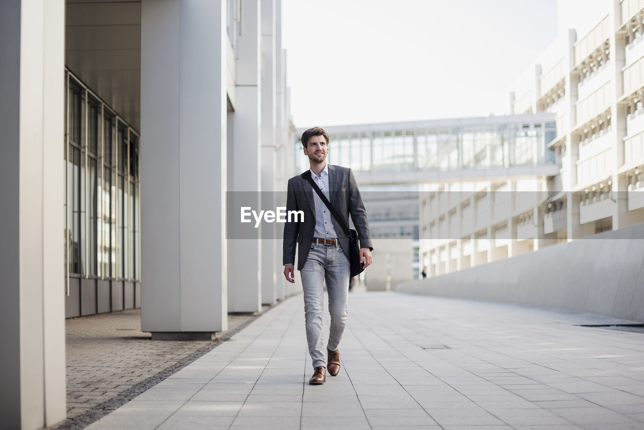 Smiling businessman with crossbody bag in the city on the move