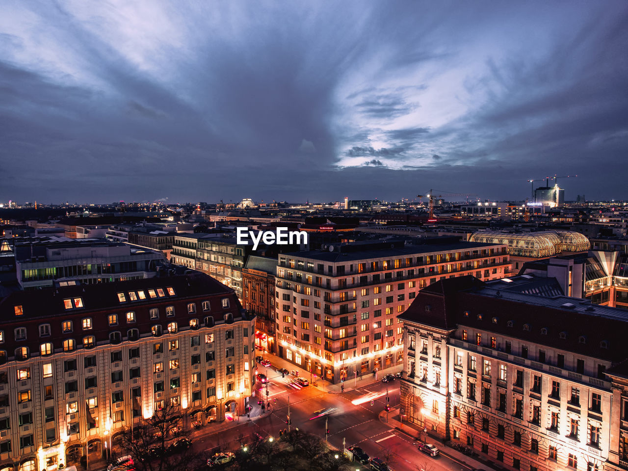 High angle view of illuminated cityscape against cloudy sky at dusk