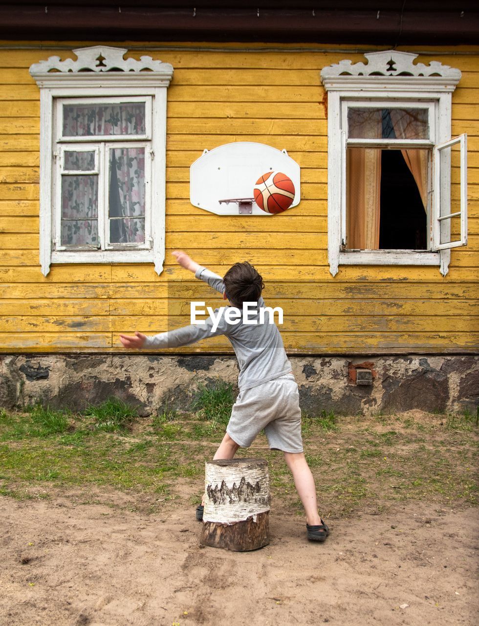 Rear view of kid playing basketball near house