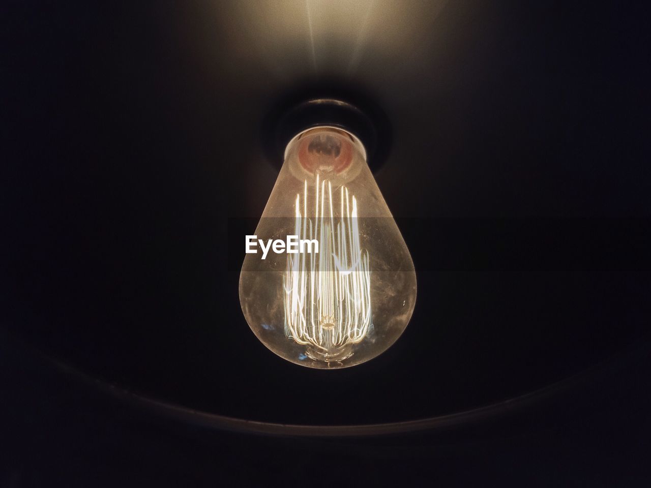 CLOSE-UP OF ILLUMINATED LIGHT BULB AGAINST BLACK BACKGROUND