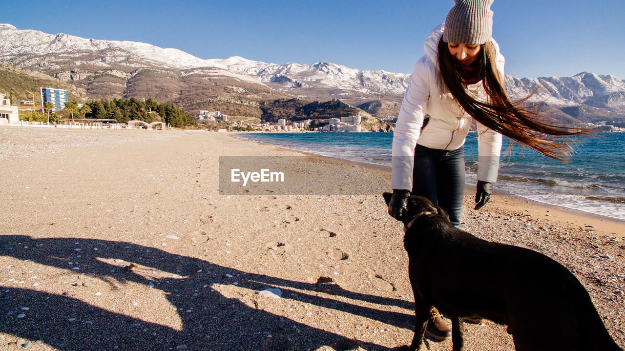 Woman with dog standing at beach against sky