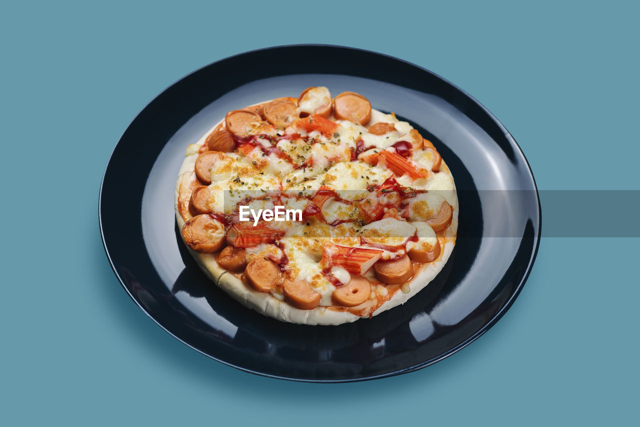 Sausage and crab stick pizza in a ceramic plate isolated on pastel colors background.