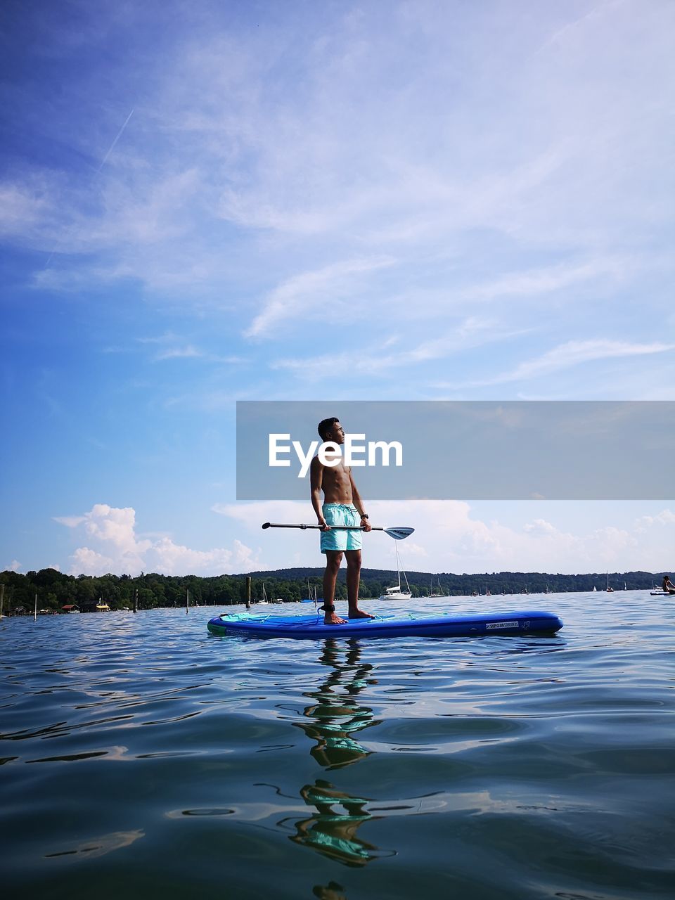 Shirtless teenage boy paddleboarding in sea against sky