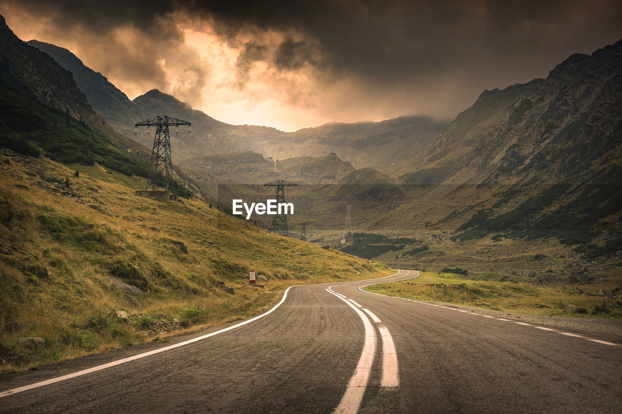 Empty road leading towards mountains against cloudy sky